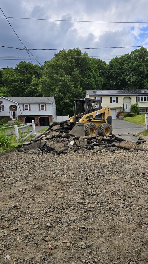 Skid steer removing an old asphalt driveway as part of a Nila-Structures driveway replacement