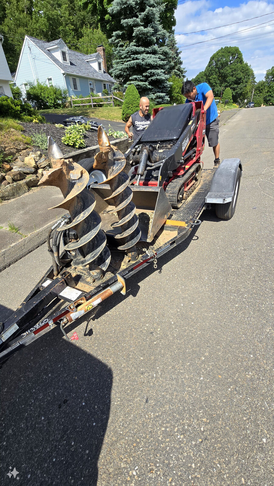 Nila-Structures crew loading a compact track loader with auger attachment onto a trailer for a residential job